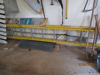 Yellow fiberglass two-section extension ladder with aluminum rungs laid horizontally in garage