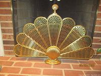 Brass peacock tail fan fireplace screen with shell base standing in front of brick fireplace
