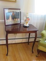 Queen Anne style wood table with curved legs supporting a ceramic floral lamp and framed poster on top
