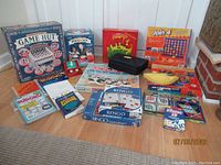 Full view of the group of games and puzzle books showing boxed games, standalone books, and a Monopoly game set spread on the floor.