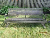 Front view of the vintage garden bench showing the wooden slats and curved cast iron frame with armrests.