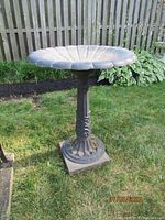 Metal bird bath with scalloped basin viewed fully from the side