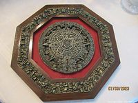 Full view of the mounted Aztec sun calendar piece with ornate wooden octagonal frame and red velvet background.