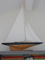 Full side view of the hand crafted wooden sailboat model showcasing black top edge, natural wood hull, and both sails.