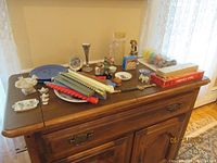 Overview of lot items arranged on wooden cabinet including candles, plates, small figurines, and novelty items.