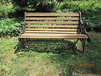 Front view of entire wood and wrought iron park bench on grass showing overall condition