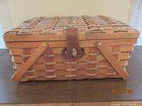 Front view of the woven picnic basket closed with a leather buckle lid.
