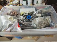 Clear plastic bin with assorted plumbing supplies including plastic piping fittings, brushes, plumbing tape, and other small parts.