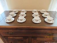 Twelve porcelain tea cups and matching saucers arranged on a wooden surface showing the full lot.