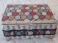 Wicker sewing basket with lid covered in colorful patchwork fabric pattern.