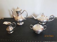 Full view of coffee pot, tea pot, sugar bowl and creamer on a black surface showing the entire set.