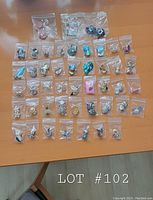 Overview of 46 pairs of clip-on earrings, each individually bagged and arranged on a wooden table showing variety in styles, colors, and shapes