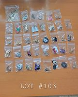 Top-down view of 38 pairs of costume jewelry earrings individually bagged and arranged in rows on a wooden surface, showing diverse shapes, colors, and styles.