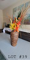 Full view of large bamboo weave vase with artificial flowers set on table indoors.