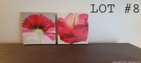 Two square canvas art pieces showing close-up red flowers, displayed side by side on a surface.