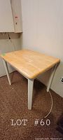 Small wood table shown from a corner angle displaying wood top and white legs