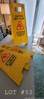 Photo showing three yellow lightweight plastic wet floor signs stacked on a table, each with bilingual caution text and slip hazard pictogram.