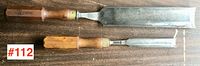 Two antique chisels with wooden handles lying on a wooden surface, shown side by side to display size difference.