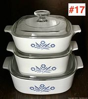 Three stacked rectangular Corning Ware casserole dishes with blue floral pattern and clear glass lids.