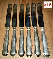 Top view of six antique butter knives with tarnished silver handles and black blades.