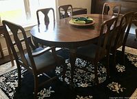 Overall view of oval dining table with Queen Anne cabriole legs along with six T-back chairs around it on a patterned rug.