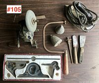 Photo showing entire lot: bench grinding wheel, angle square set in box, vintage iron, two lead plumb weights, chisels, and scrapers on wooden surface.