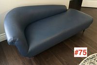 Front angled view showing the curved backrest and one-armed design with smooth blue faux leather upholstery.