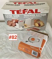 Tefal electric slicer with original box and Neatfreak retractable clothesline box in foreground, displayed on a white quilted surface.