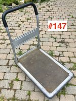 Side angled view of the folding box cart showing the handle, platform surface, and wheels.