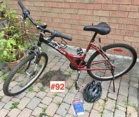 Full side view of the ladies' Raleigh 18 speed mountain bicycle showing red and black frame, 26 inch tires, helmet and book on ground.