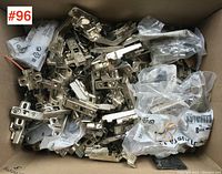 Box filled with multiple metal cabinet door hinges and several small plastic bags containing screws and mounting hardware.