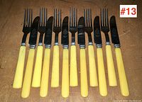 Photo of 6 forks and 6 knives with yellow handles arranged side by side on a brown surface. Shows the full set and condition of handles and metal parts.