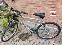 Full side view of men's mountain bicycle with silver frame, black tires, and yellow/black detailing, against a brick wall.