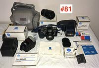 Overview of Minolta Maxxum camera set including camera body, two lenses, flash unit, camera bag, lens caps, manuals, and accessories arranged on a white surface for full lot display.