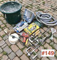 Overview photo of plastering and drywall tools arranged on cobblestone pavement showing bucket, sprayer, drill, paddles, and hand tools.