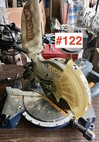 Front angled view of Ryobi compound mitre saw showing blade, angle scale, base, and dust collection bag.