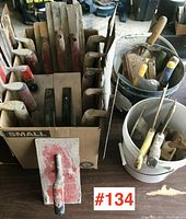 Box filled with plaster, concrete, and stucco trowels showing different handle types and blade shapes.
