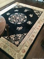 Overall view of black-ground rug under dining table on hardwood floor