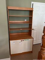 Front view of wood bookcase showing three shelves and lower cabinet with white doors and wood knobs.