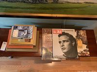 Photo showing stack of 9 books, mix of hard and softcover, with art and travel themes. Includes 'Halsman A Retrospective' and 'America The World of the 1930s'.