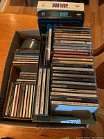 Top view of the box containing multiple CDs, some in jewel cases and some boxed sets, mostly classic rock and soul genres.