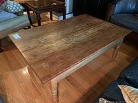 Photo of the vintage hardwood coffee table showing the top surface and turned legs on a hardwood floor setting.