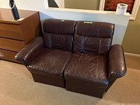 Front view of two-seat brown leather couch with armrests, showing worn leather and creases.