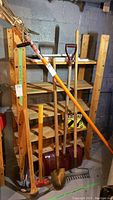 Wide view photo showing garden tools including limb trimmer, rake, snow shovel, spade, sledgehammers leaning against wooden shelves