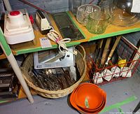 Wide shot showing basket with cutlery, orange nesting bowls, electric slicer and mandolin slicer on shelf, glassware on table