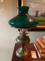 Vintage oil lamp with brass base, clear glass chimney, and green glass shade with white interior collar shown in upright position.