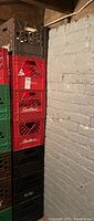 Stack of seven assorted plastic milk crates in red, brown, green, and black, some marked with Sealtest branding.