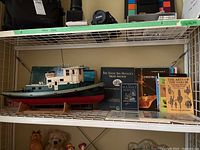 Wide side view of shelf showing the model boat replica of the Esso Honduras tug boat with six nautical-themed books behind it.