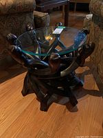 Side angle view showing full wooden base with human figures and round glass top set on wooden figures' heads and limbs.
