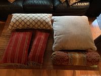 All five pillows arranged on a wooden table in front of a dark leather couch showing different sizes and designs.